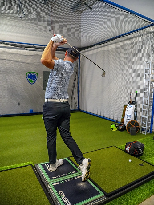 Golfer practicing full swing on a performance training platform at Elevate Golf indoor facility.
