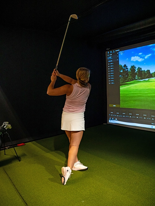 Golfer practicing full swing inside Elevate Golf simulator during the Summit Training Program.